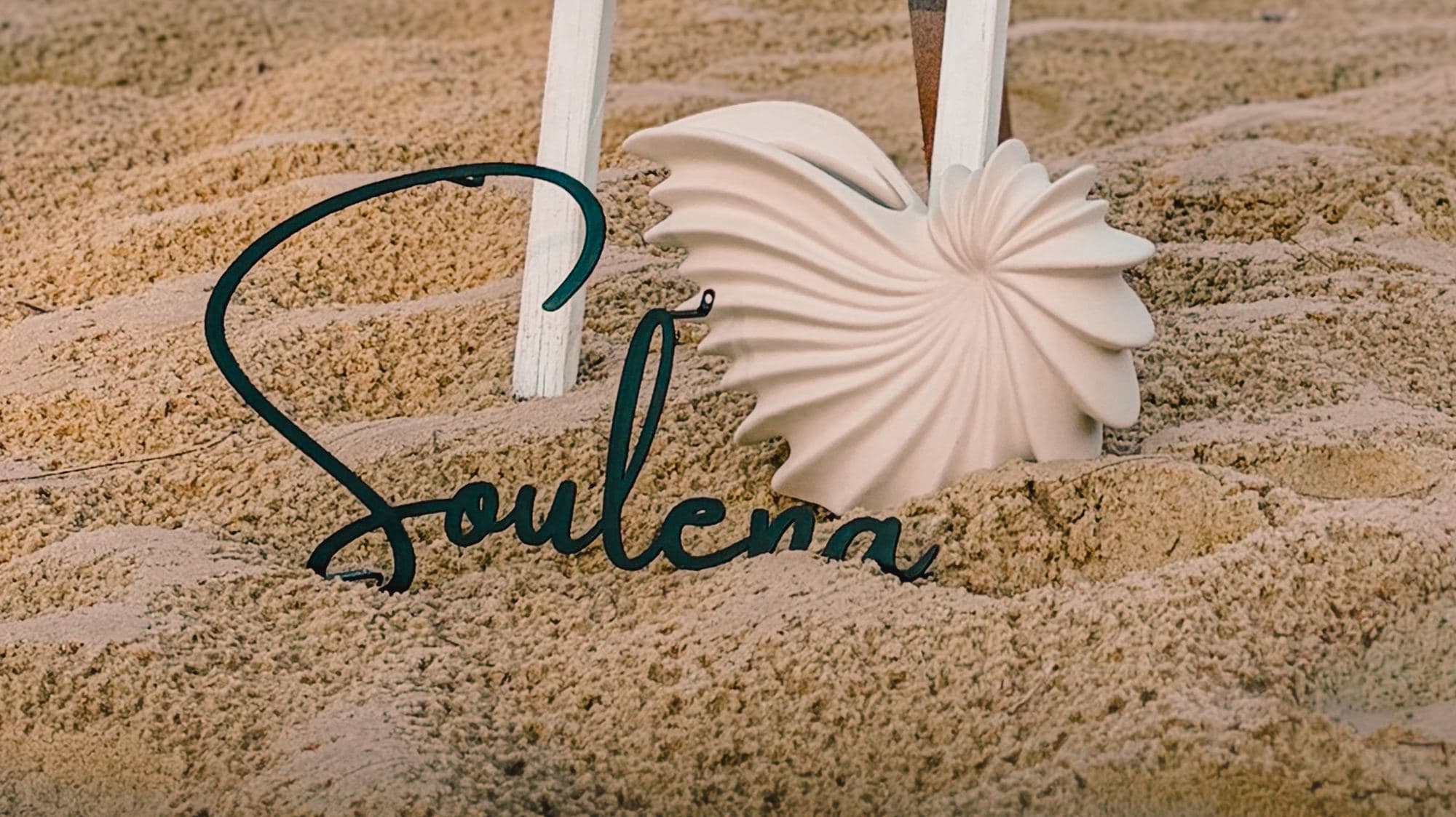 Soulena's flower mark resting in the sand beside the beach yoga sign